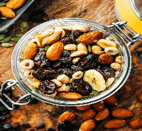 Apartments For Rent Midtown Houston A glass jar filled with a mix of dried fruits, nuts, and cereal sits on a wooden surface. Loose almonds and raisins are scattered around the jar.